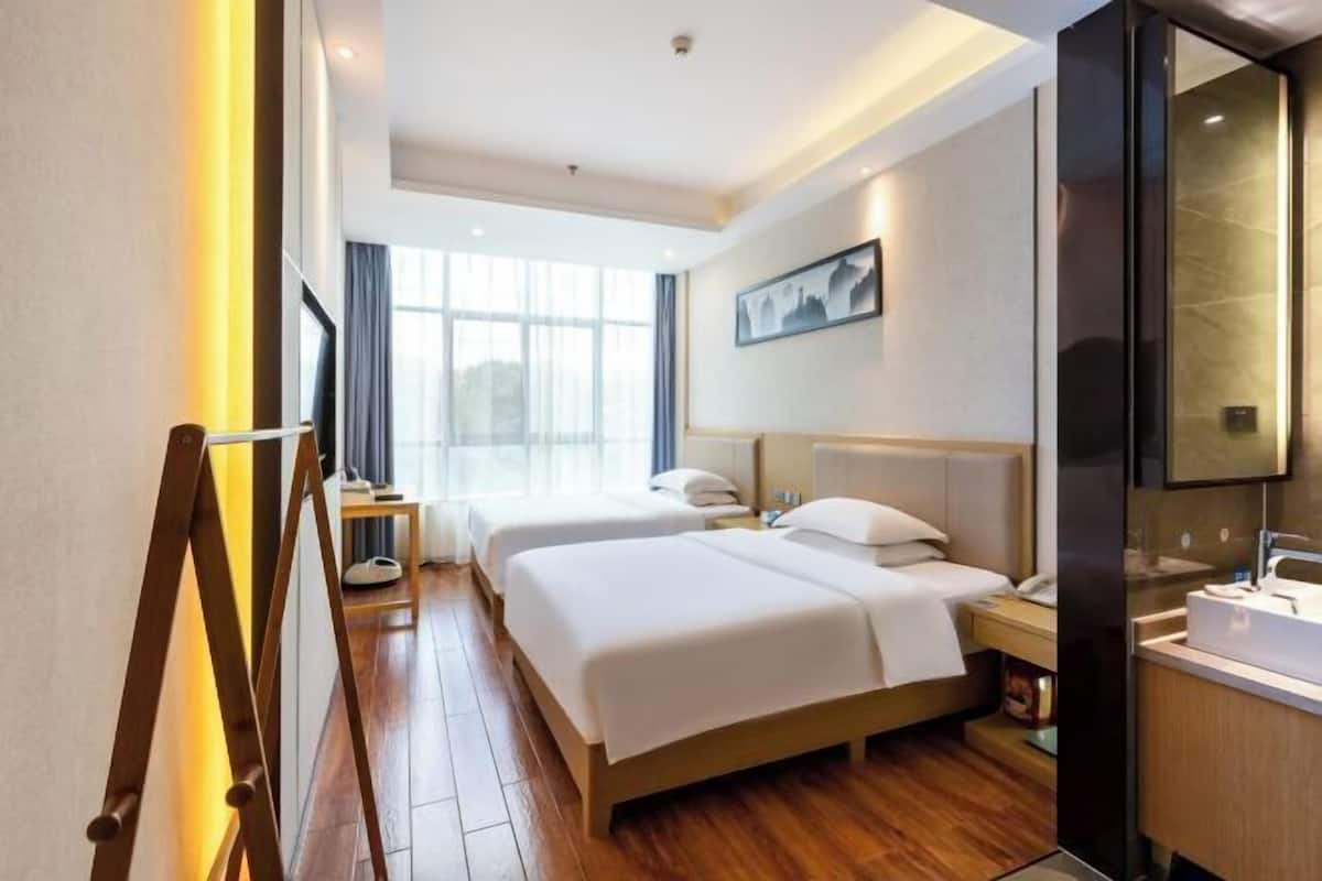 Ein Hotelzimmer mit zwei Betten, einem großen Fenster, einem Bild an der Wand und einem modernen Badezimmer.