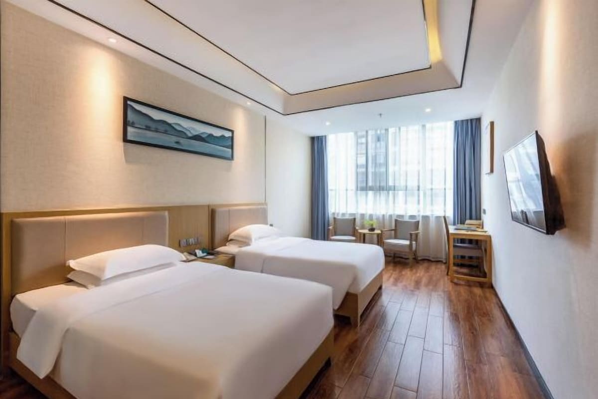 A hotel room with two beds, a desk, a chair, a TV, and a window with curtains.