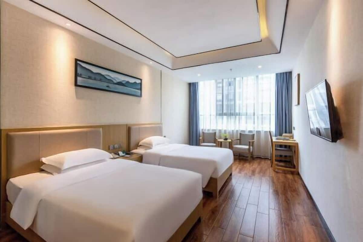 Ein Hotelzimmer mit zwei Betten, einem Schreibtisch, einem Stuhl, einem Fernseher und einem Fenster mit Vorhängen.