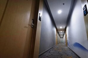 Un couloir d’hôtel avec une porte en bois, un interrupteur et un panneau fixé au mur.