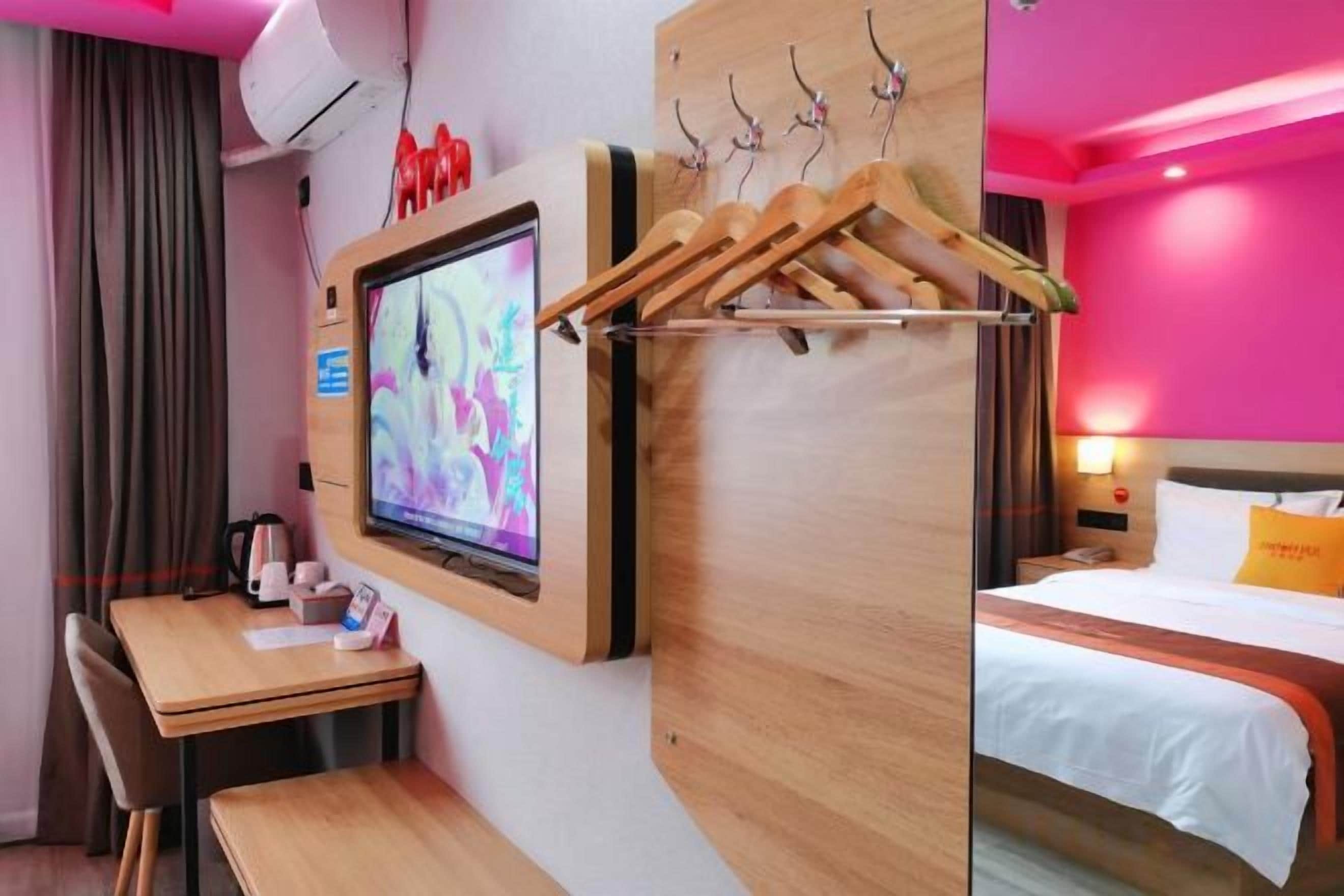 A hotel room with a TV, wooden furniture, a bed, and a wall-mounted coat rack.