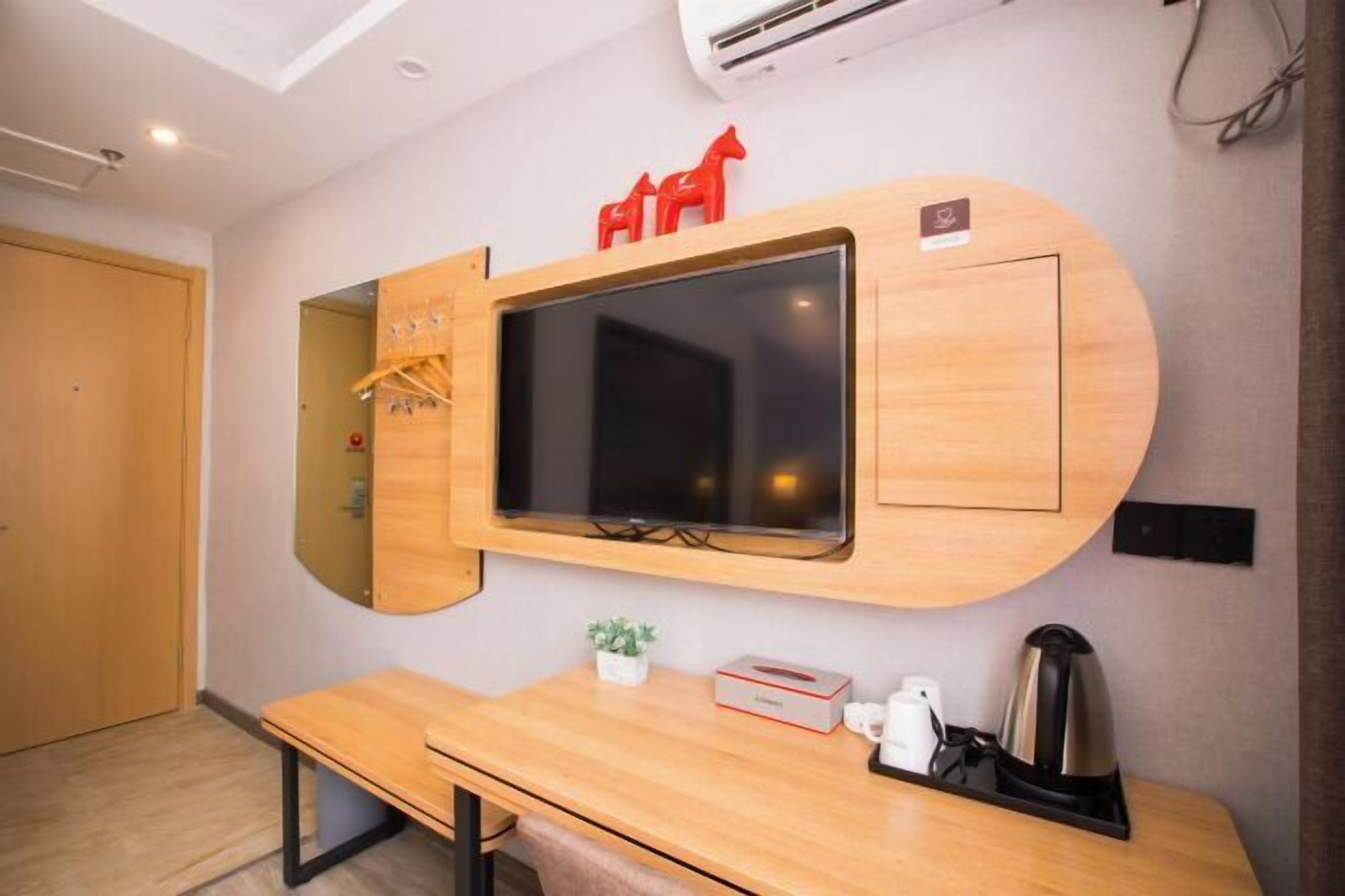 Una habitación de hotel moderna con un tocador de madera, un espejo grande, un televisor de pantalla plana, una planta pequeña y una cafetera.