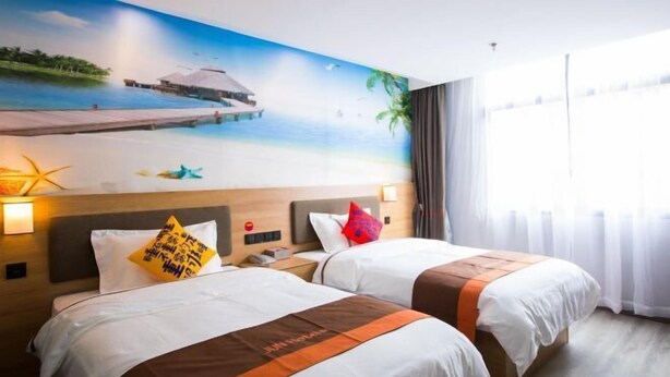 Habitación de hotel con dos camas, un mural con escena de playa y vista al mar.