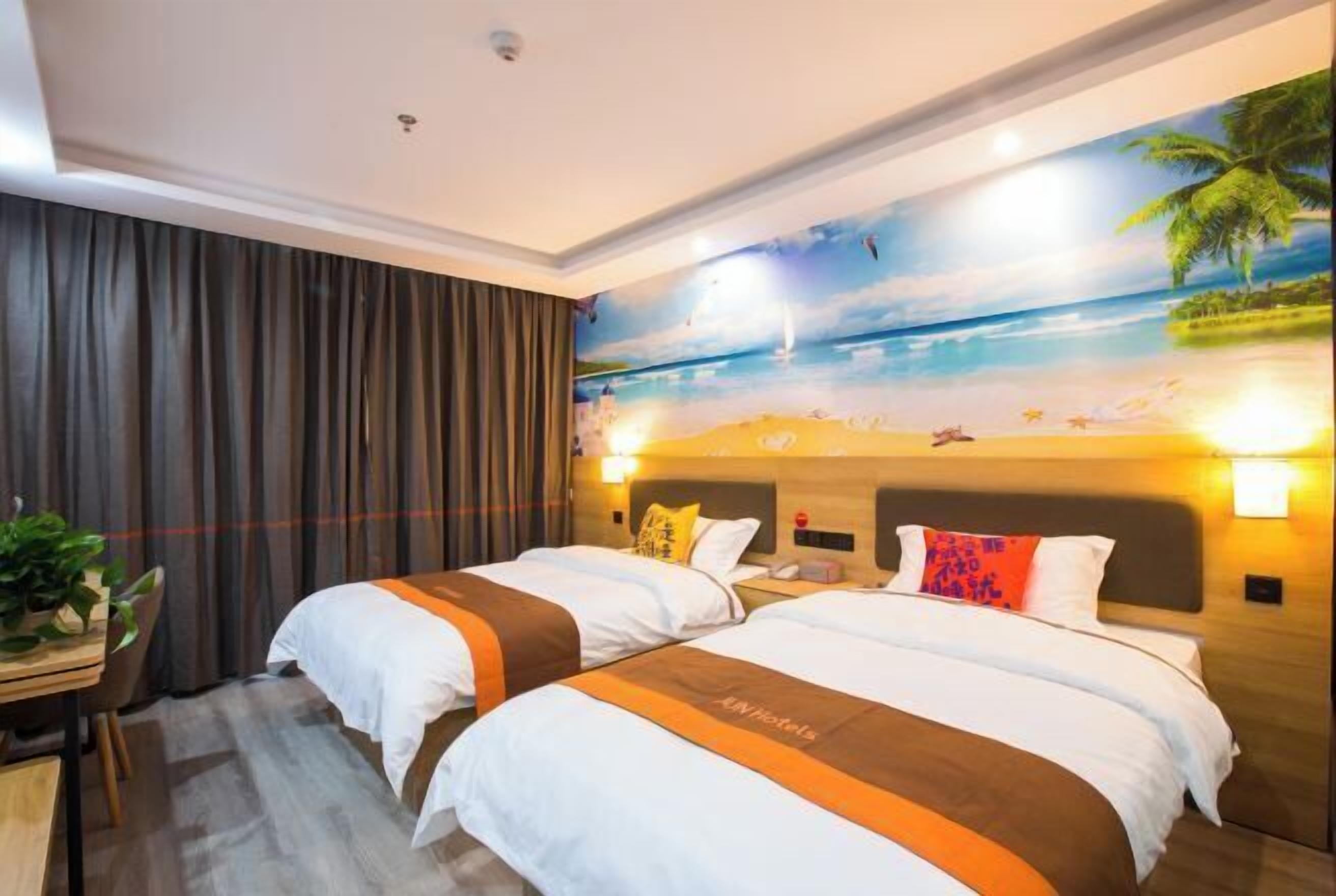 Une chambre d’hôtel avec deux lits, une fresque représentant une scène de plage et un bureau agrémenté d’une plante.