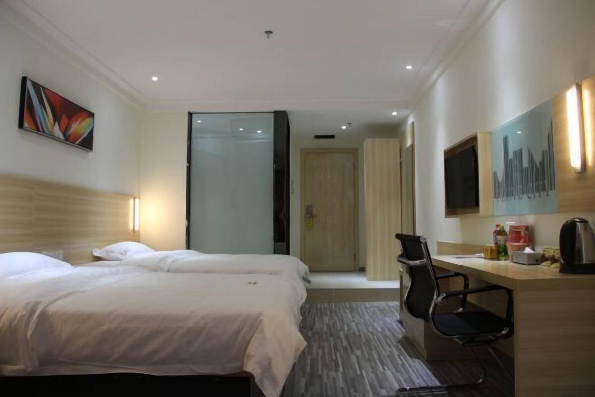 A hotel room with two beds, a desk with a chair, a television, and a door leading to another room.