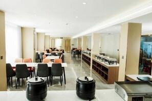 Un comedor moderno con varias mesas y sillas, una barra larga con equipo de servicio de alimentos, y un ambiente limpio y bien iluminado.