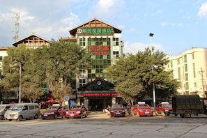 Un hotel con un letrero visible, un estacionamiento con varios coches y edificios circundantes.