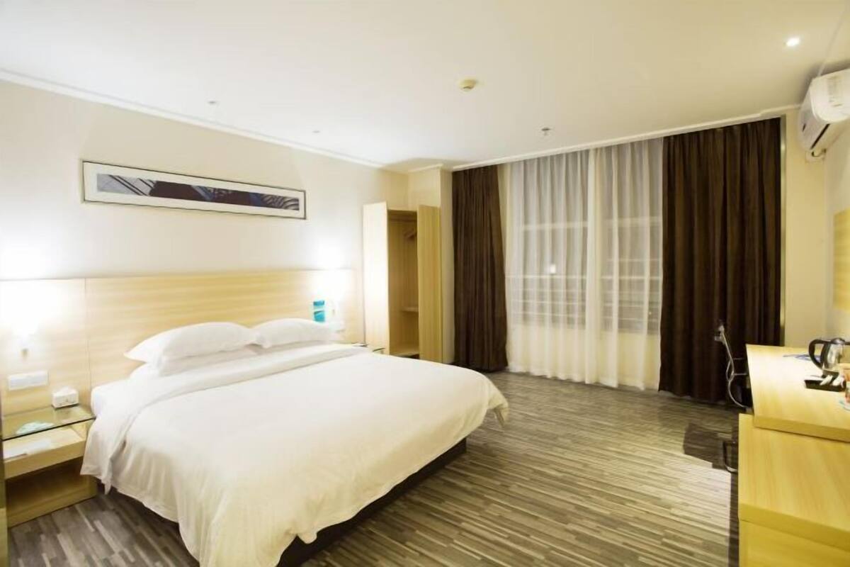 A hotel room with a bed, bedside table, and a desk with a chair.