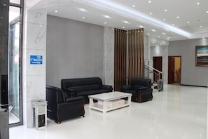 Un lobby moderno con una pared de mármol, dos sofás negros, una mesa de centro blanca y una escalera.