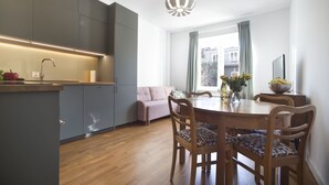 A modern kitchen with grey cabinets, a wooden dining table with chairs, and a pendant light. - P&O Apartments Gdańska (Warsaw)