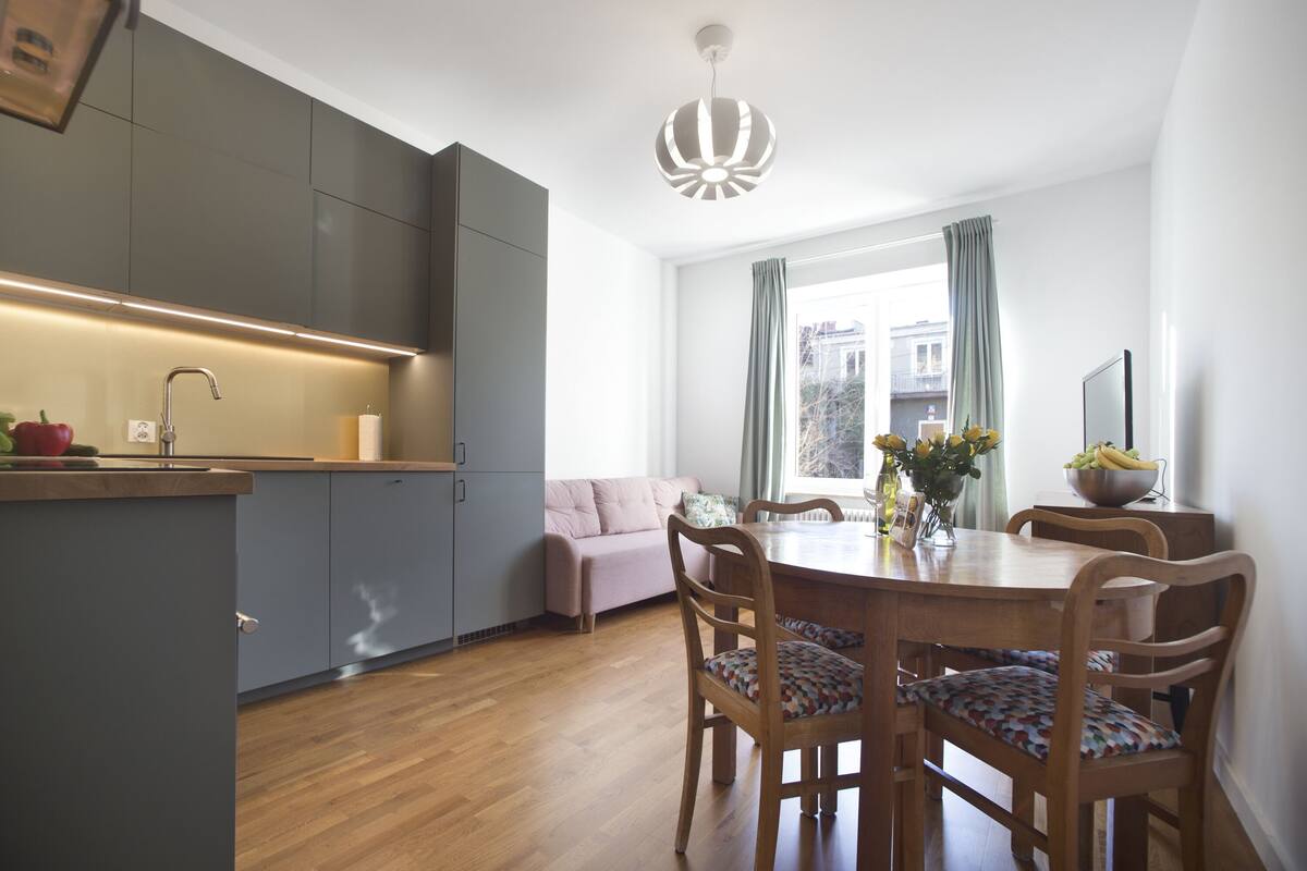 Una cocina moderna con armarios grises, una mesa de comedor de madera con sillas y una lámpara colgante.