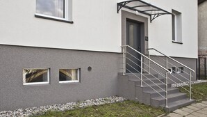 A modern building with a grey facade, a set of metal stairs with a glass balustrade, and a small window with a view of trees. - P&O Apartments Gdańska (Warsaw)