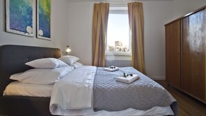 A neatly made bed with white linens, a wooden wardrobe, and two abstract paintings on the wall. - P&O Apartments Gdańska (Warsaw)