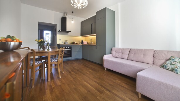 A modern kitchen with wooden cabinets, a dining table with chairs, and a light-colored sofa. - P&O Apartments Gdańska (Warsaw)