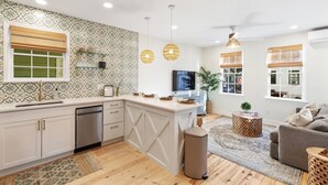 A modern kitchen with a central island, a dining area with a sofa, and a TV. - The Charleston Suites: The Victoria Suite - 3bd/2ba ample outdoor space (Charleston)