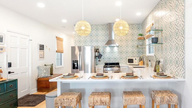 A modern kitchen with a central island, bar stools, hanging pendant lights, and patterned wallpaper. - The Charleston Suites: The Victoria Suite - 3bd/2ba ample outdoor space (Charleston)