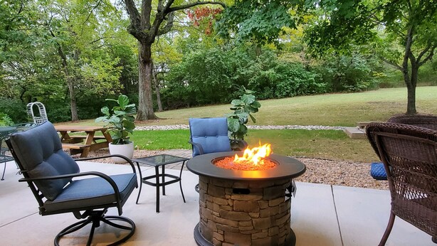 An outdoor patio area with a stone fire pit, seating, and a view of a grassy yard. - Peaceful retreat, just 10 minutes outside of town (LAWRENCE)