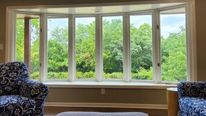 A room with a large bay window overlooking a lush green landscape. There are two patterned armchairs and a small ottoman. - Peaceful retreat, just 10 minutes outside of town (LAWRENCE)
