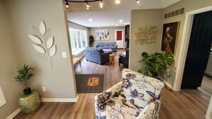 A spacious living area with a sofa, a coffee table, and a potted plant. There is a door leading to another room with a bench and a window. - Peaceful retreat, just 10 minutes outside of town (LAWRENCE)