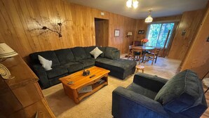 Un salon chaleureux avec un mur lambrissé en bois, un canapé vert foncé, une table basse en bois et un fauteuil bleu.