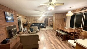 Un salon spacieux doté d’une cheminée, d’un ventilateur de plafond et d’un coin repas avec des meubles en bois.
