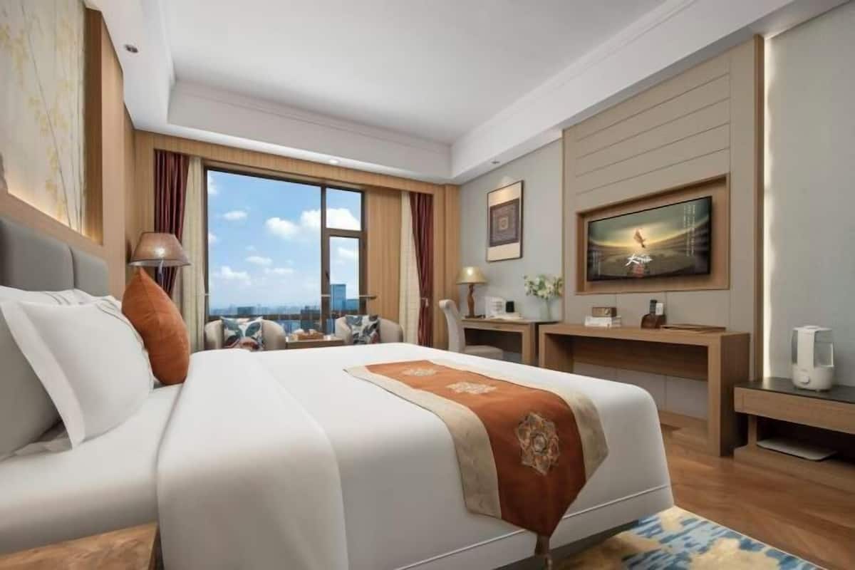 Habitación de hotel con una cama grande, un escritorio, un televisor y vistas a la ciudad.