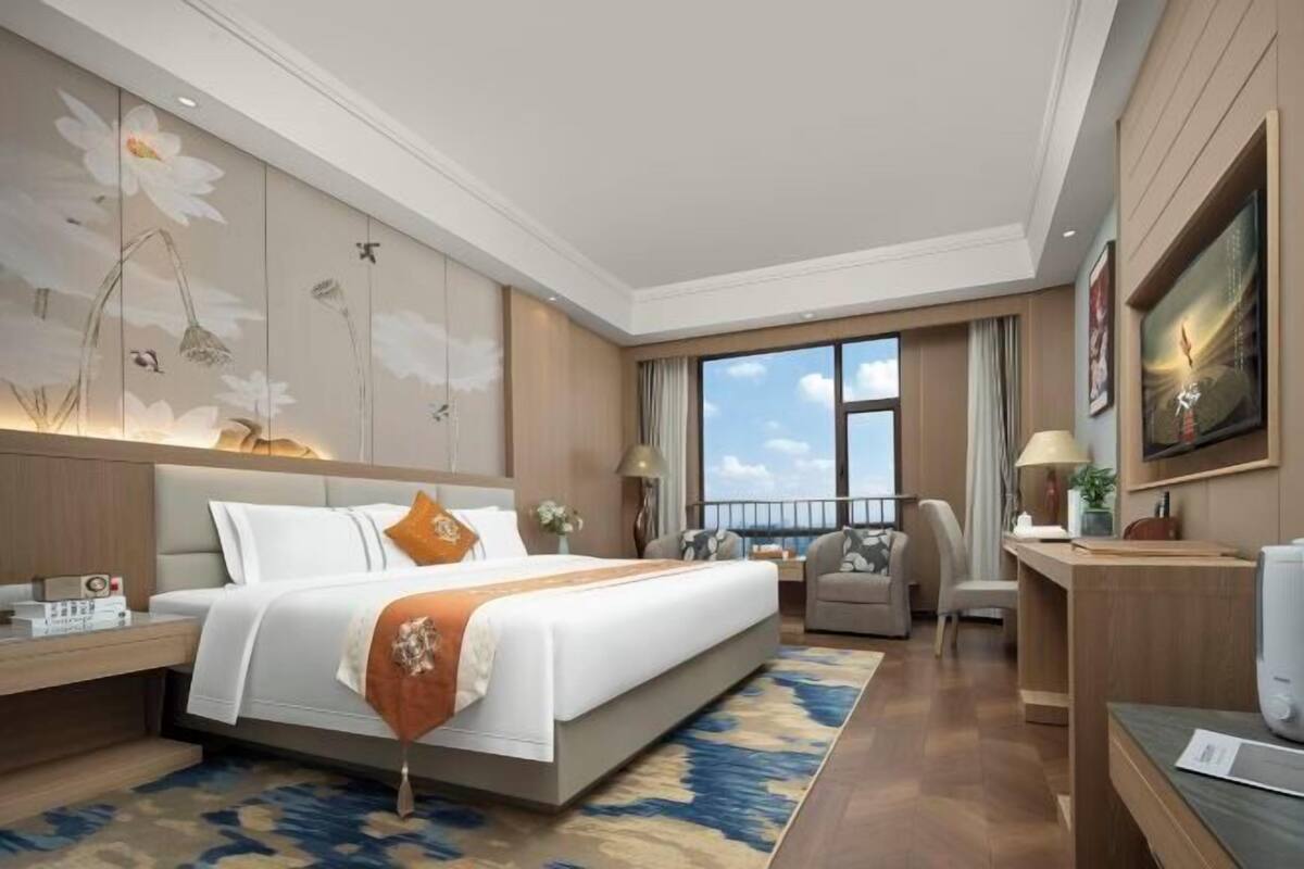 Habitación de hotel con una cama grande, un escritorio, una silla y vista al cielo.