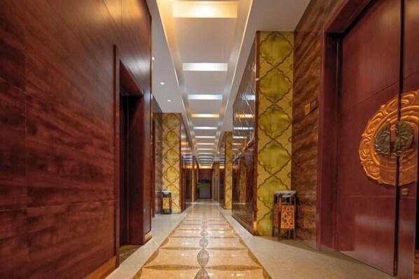 Un pasillo de hotel con paneles de madera, suelo de mármol y una pared decorativa con un emblema dorado.