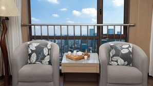 A room with two armchairs, a small table with a tray of items, and a view of the city through large windows. - Yulin Hotel (Guazhou)