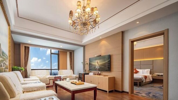 A hotel room with a large window, a chandelier, a flat-screen TV, and a bed. - Yulin Hotel (Guazhou)