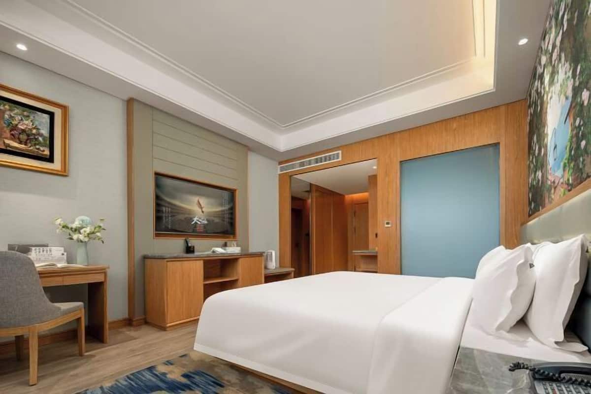 Habitación de hotel con cama, escritorio, silla, televisor y un cuadro en la pared.