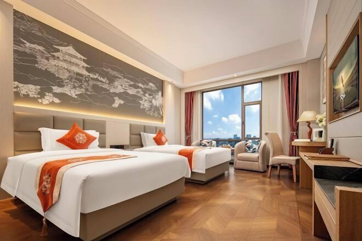 Habitación de hotel con dos camas, un sofá, un escritorio y un ventanal con vistas a la ciudad.