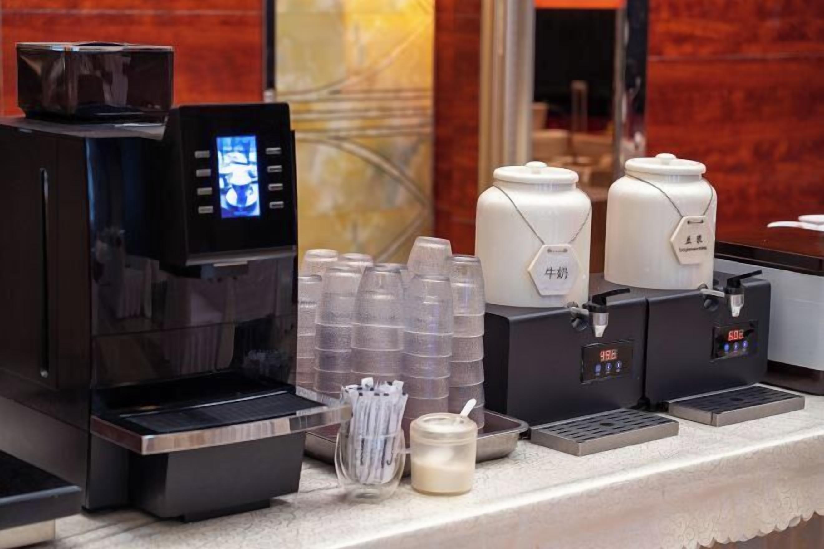 A coffee station with a digital coffee machine, disposable cups, and a milk dispenser.
