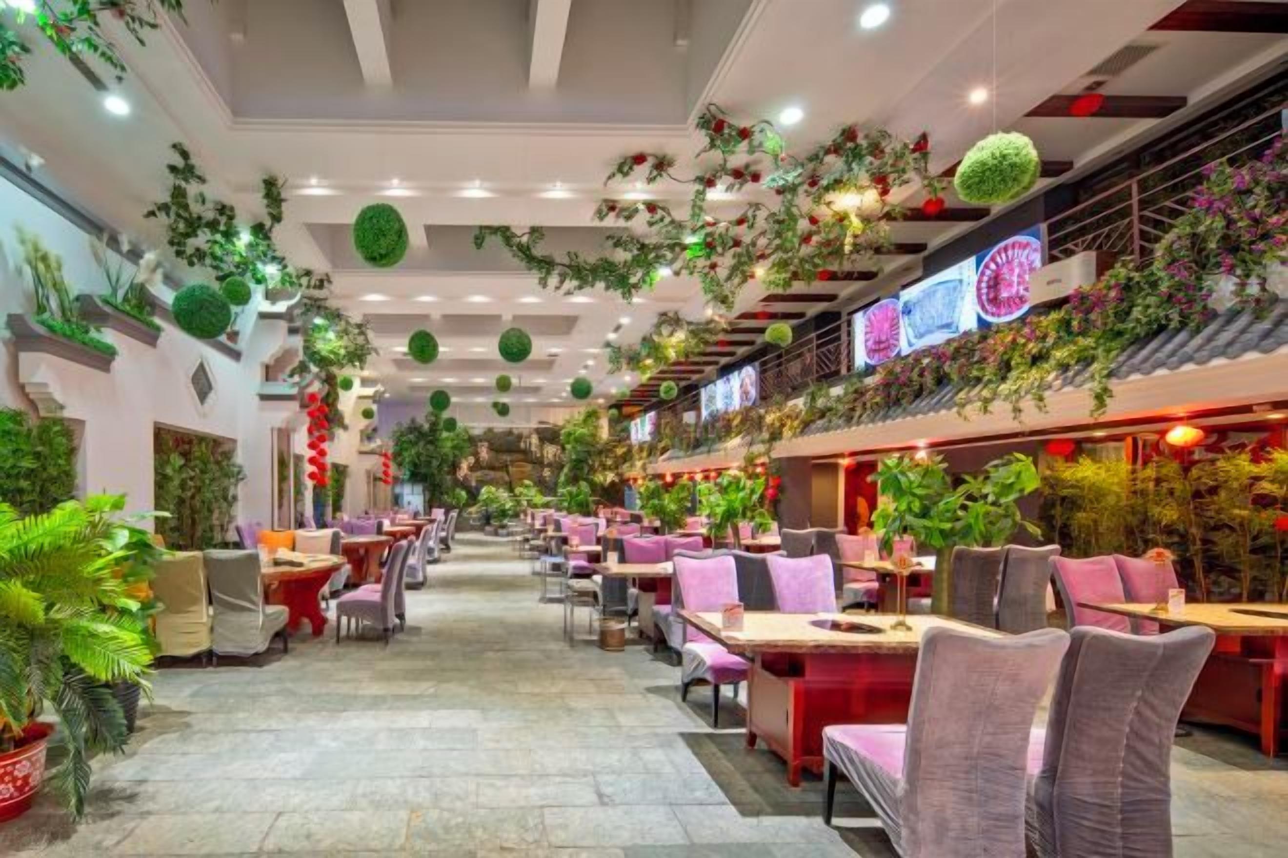 A spacious indoor dining area with multiple tables and chairs, ceiling plants, and a variety of hanging decorations.