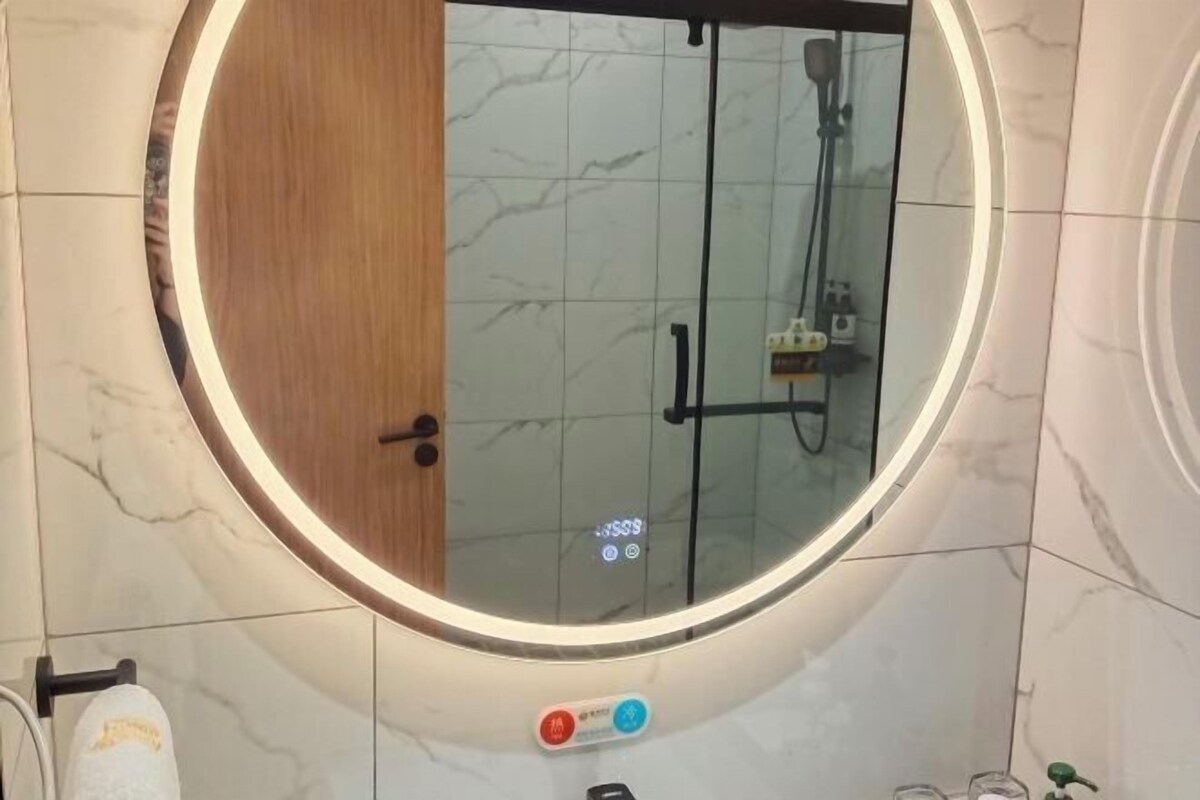 A bathroom with a round mirror, a wooden door, and a glass shower enclosure.