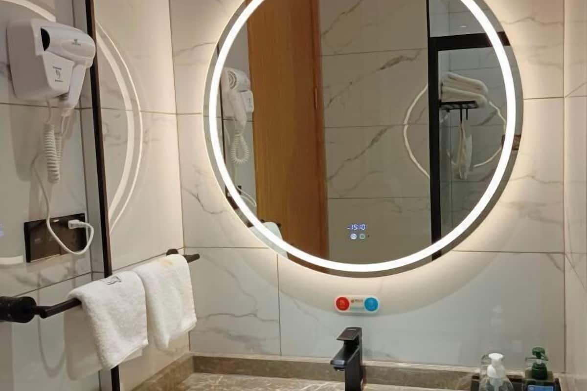 Un baño con un espejo redondo, un secador de pelo, un perchero y un secamanos.
