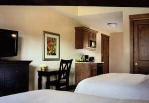 Ein Hotelzimmer mit zwei Betten, einem Esstisch mit Stühlen, einer kleinen Küchenzeile und einem Fernseher.