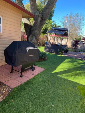 Un patio trasero con una parrilla cubierta, cerca de madera y una zona de patio.