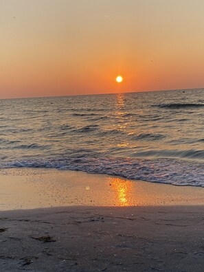 A beach at sunset with the sun reflecting on the water.