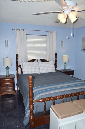 A bedroom with a wooden bed, two bedside tables with lamps, a ceiling fan, and a window with blinds.