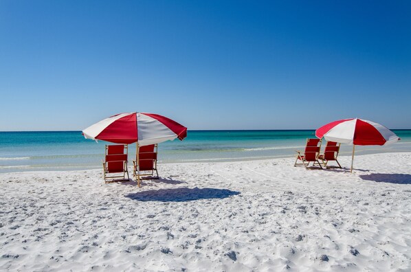 A beach with two red and white umbrellas and beach chairs.