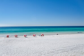 A beach with white sand and clear blue water. There are several red and white umbrellas and lounge chairs. - NEW KITCHEN! BeachFront, Bch Svc, pool, grill, kitchen, wifi (Miramar Beach)