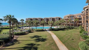 A hotel with multiple balconies, a swimming pool, and palm trees. - NEW KITCHEN! BeachFront, Bch Svc, pool, grill, kitchen, wifi (Miramar Beach)