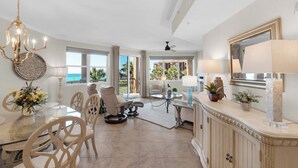 A spacious room with a dining area, a large window offering a view of the ocean, a ceiling fan, and a decorative chandelier. - NEW KITCHEN! BeachFront, Bch Svc, pool, grill, kitchen, wifi (Miramar Beach)