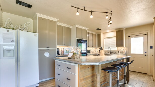A kitchen with a central island, bar stools, a refrigerator, and a built-in oven.