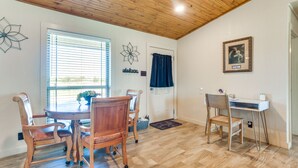 A dining area with a wooden table and chairs, a window with blinds, a door with a curtain, and a desk with a chair.