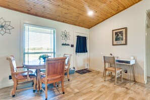 A dining area with a wooden table and chairs, a window with blinds, a door with a curtain, and a desk with a chair.