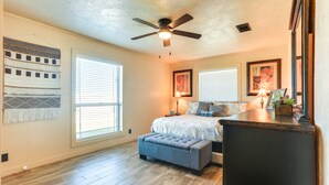 A bedroom with a bed, a ceiling fan, a bench, and a dresser.