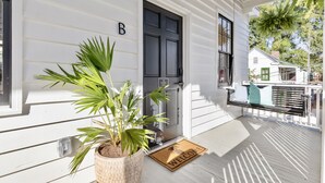 A white house with a black door, a welcome mat, and a potted plant on the porch.