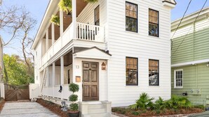A two-story house with a front porch, a wooden door, and a small front yard with plants.